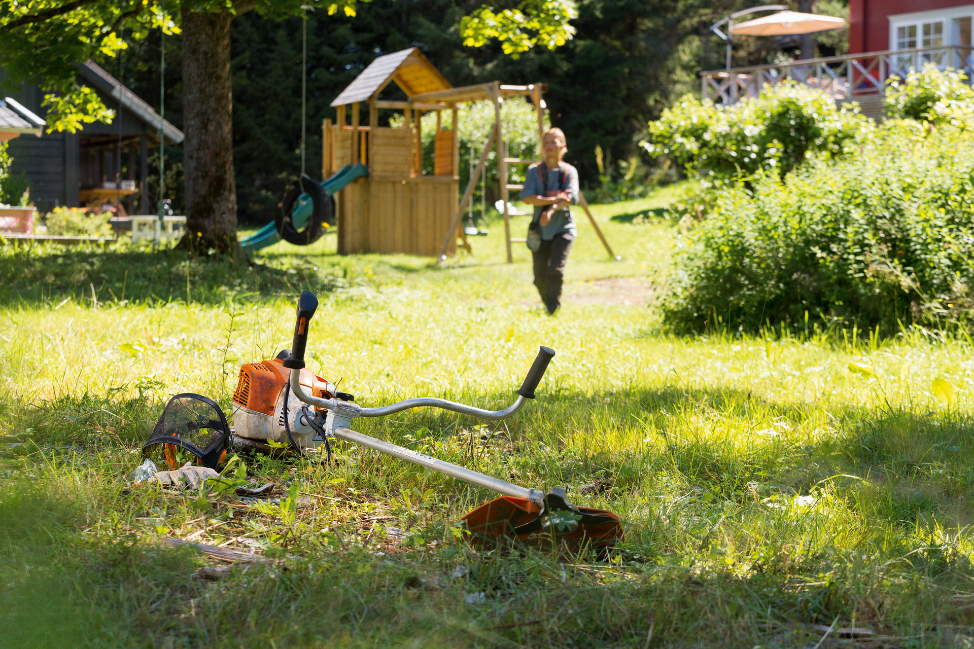 STIHL FS 240 trimmer ligger i gräset, i bakgrunden förbereder en man för underhåll