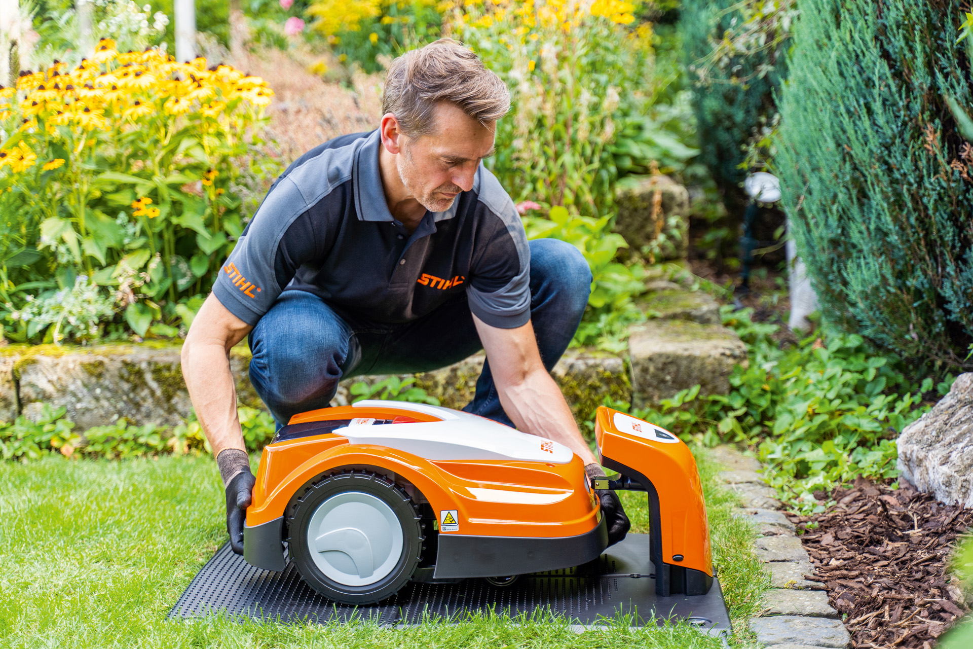 En STIHL-återförsäljare placerar en STIHL iMOW robotgräsklippare i sin laddstation i en trädgård